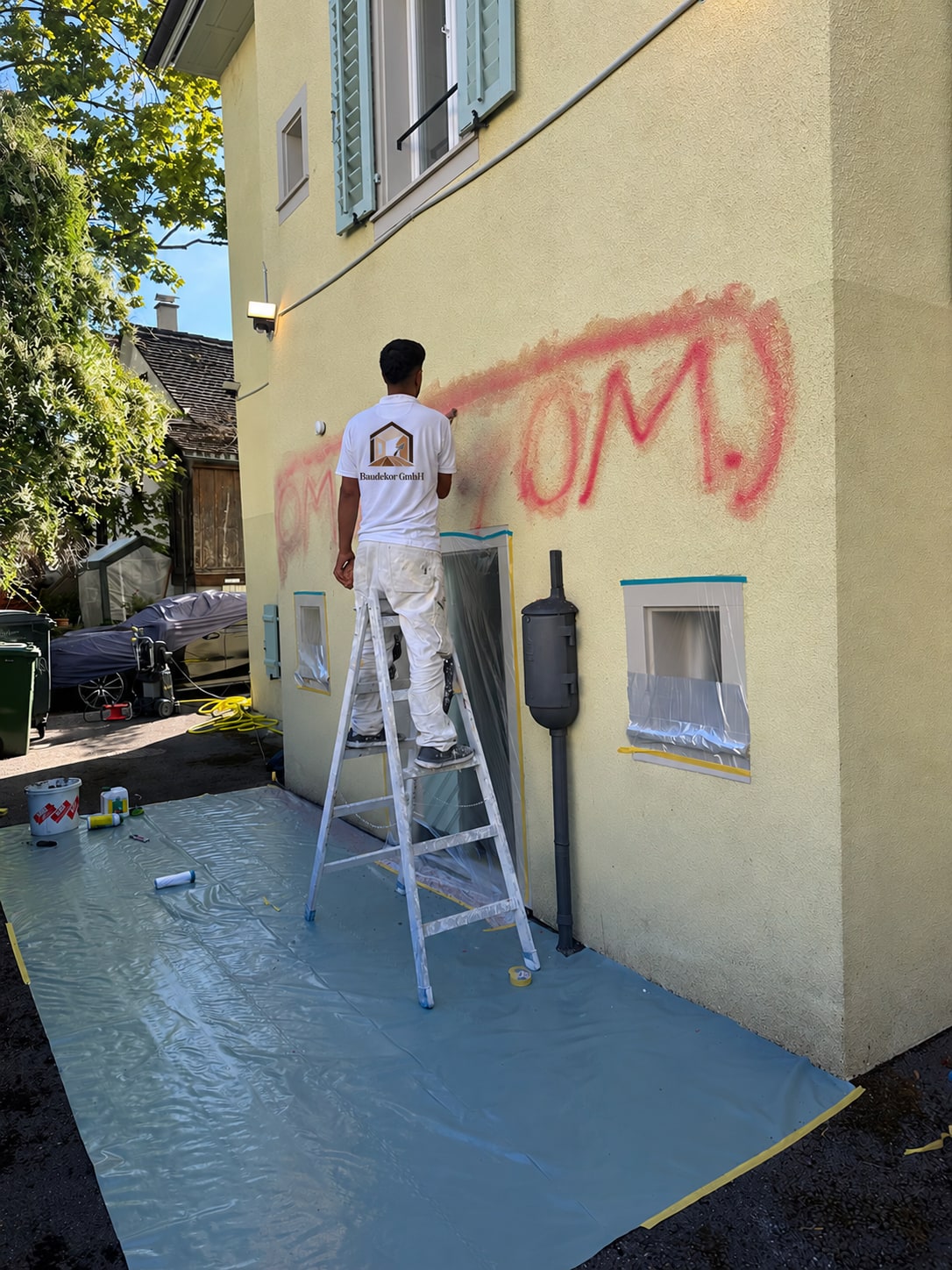 Baudekor-Mitarbeiter bei Arbeiten an einer gelben Fassade mit rotem Graffiti und abgedeckten Fenstern